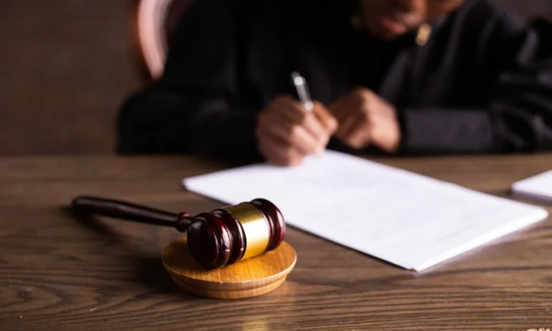 a gavel on a table with a person signing a white piece of paper.