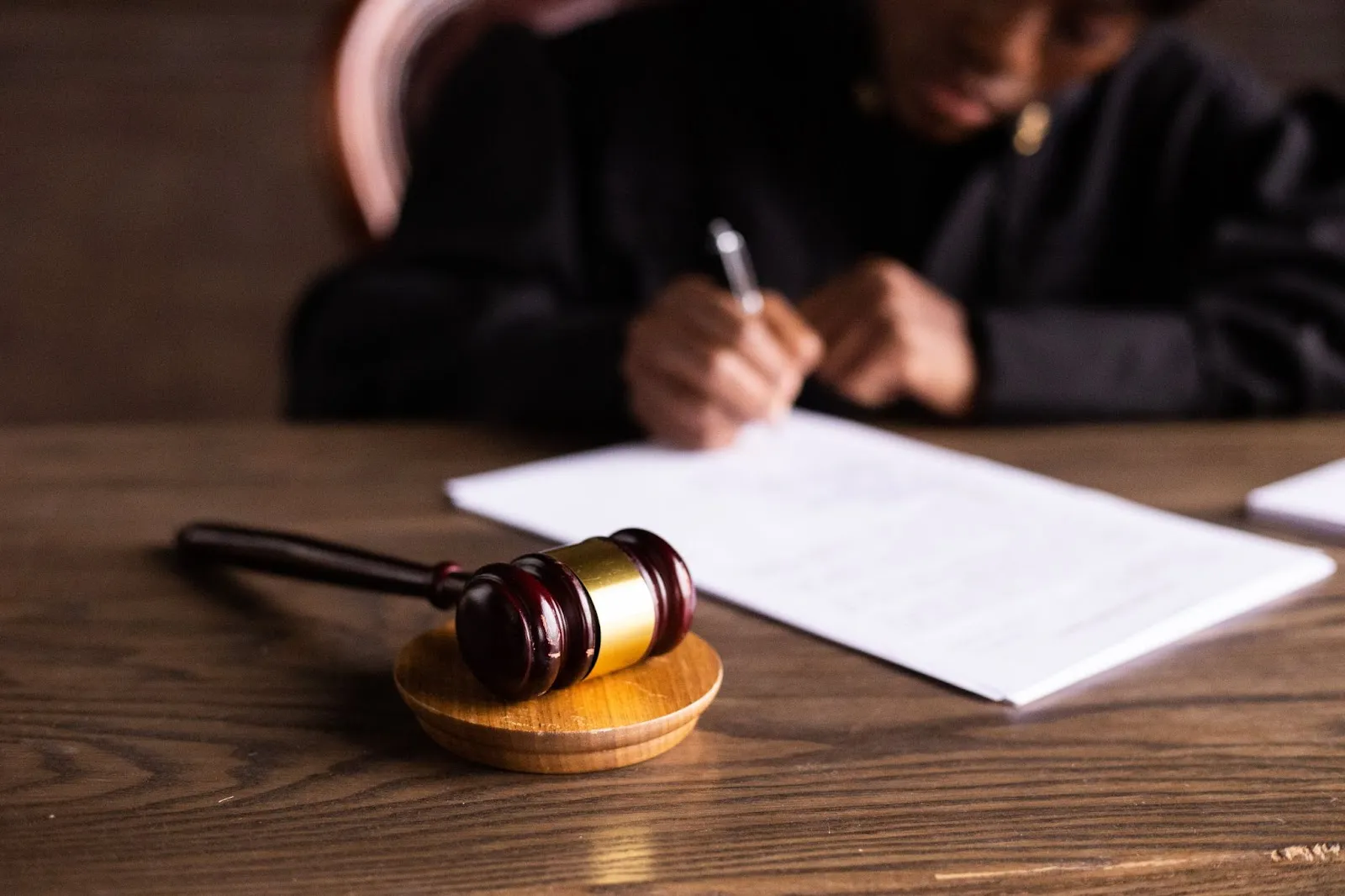 a gavel on a table with a person signing a white piece of paper.