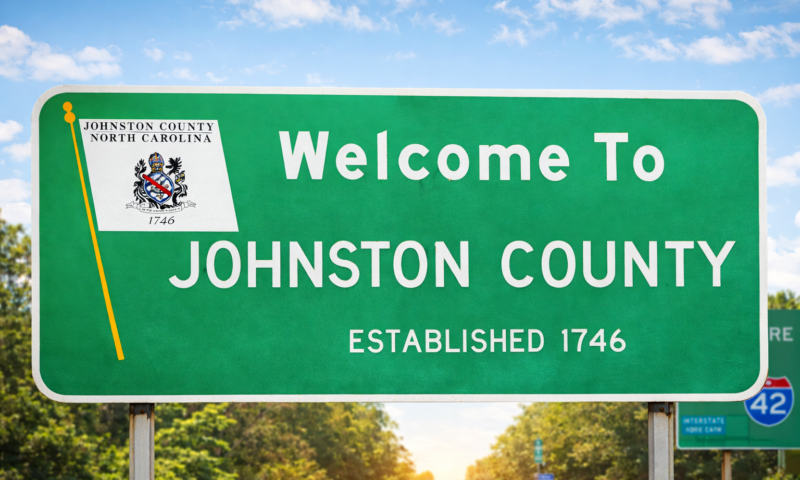 Green roadside welcome sign for Johnston County, North Carolina, reading “Welcome to Johnston County, Established 1746,” against a blue sky.