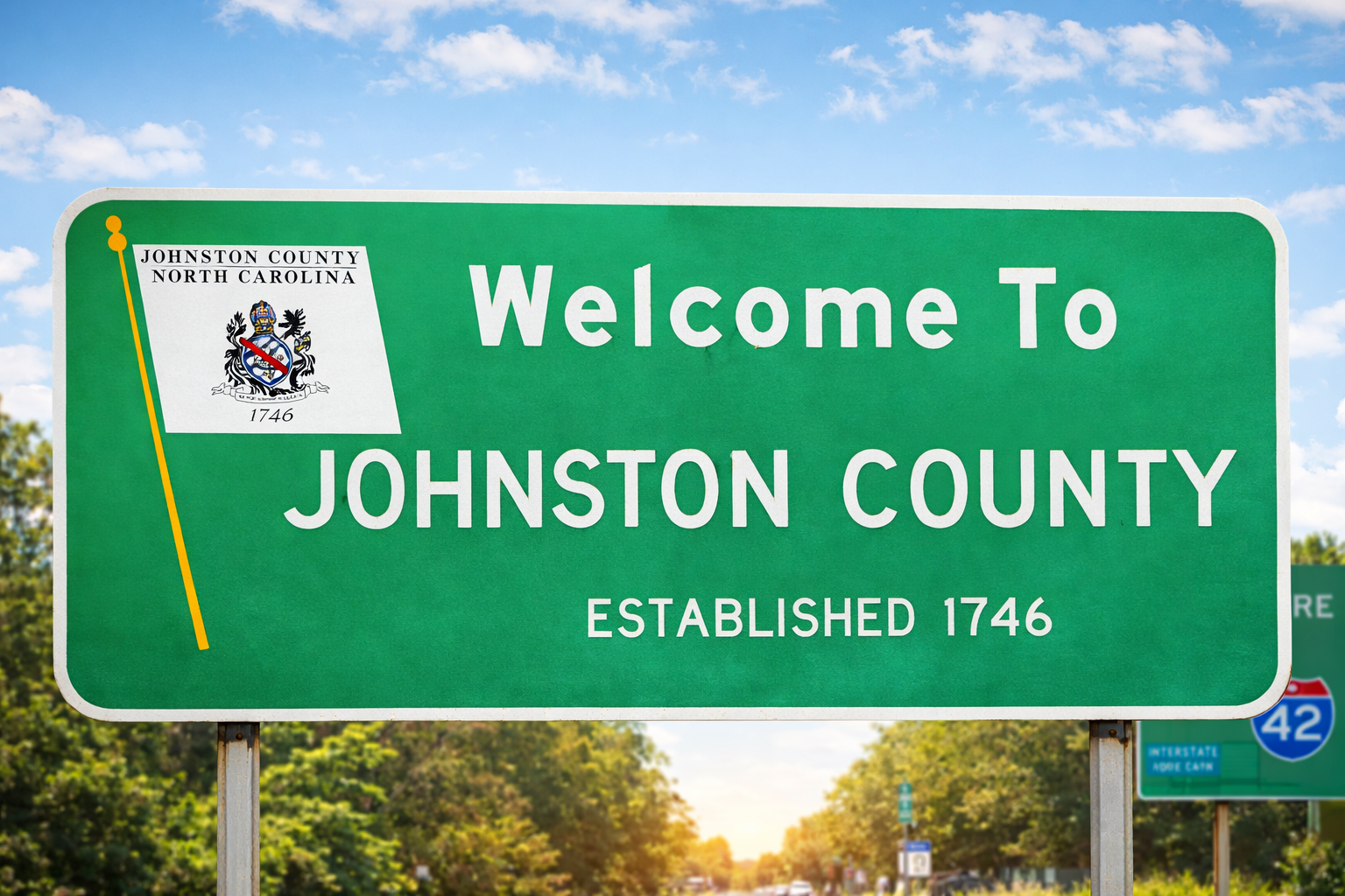 Green roadside welcome sign for Johnston County, North Carolina, reading “Welcome to Johnston County, Established 1746,” against a blue sky.
