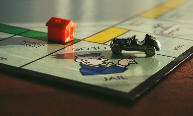 A monopoly board game with a red house and silver car. placed on the Go to Jail space.