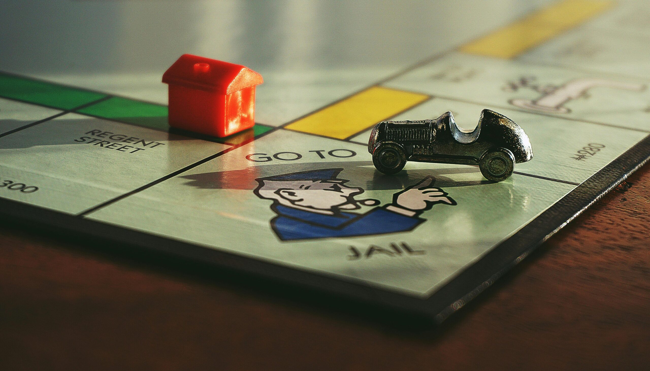 A monopoly board game with a red house and silver car. placed on the Go to Jail space.